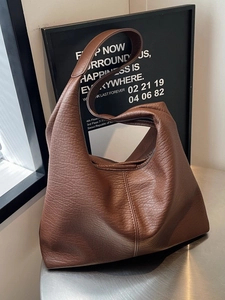 Grand sac hobo marron foncé en cuir grainé posé sur une table ronde en métal