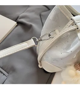 Detail of silver satin bucket bag with rivets, metal buckle and white plush pompom charm