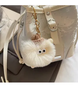 Detail of cream plush charm with big eyes and brown knit hat on a bucket bag