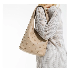 Détail du sac cabas beige avec clous floraux 3D porté à l'épaule du mannequin