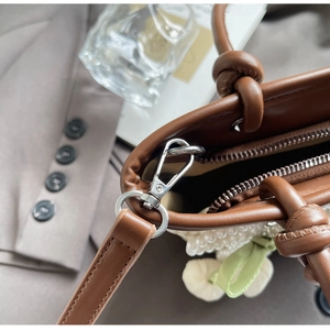 Detail of brown leather bucket bag showing silver metal hooks and pearl flower decor