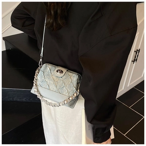 Detail of light blue crossbody bag with pleated texture and silver chain strap on model