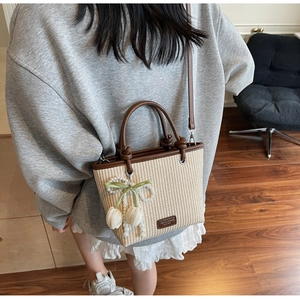 Detail of straw tote bag with pearl bow, tulip charm, and brown leather handles