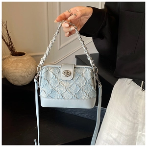 Detail of light blue quilted bag with silver chain and leather strap held by a model