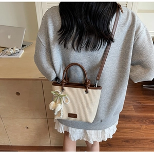 Detail of straw woven bucket bag with brown leather trim and tulip pearl pendant charm
