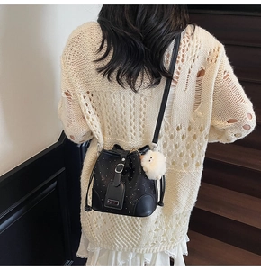 Detail shot of a black bucket bag with silver studs and a cute white plush pendant