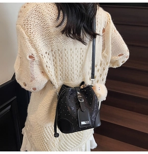 Detail of black rivet bucket bag with sheep charm worn over a white knit top