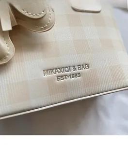 Dettaglio della pelle beige a quadri con goffratura del logo MIKAXIQI & BAG