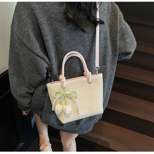 Detail of beige straw bucket bag with pink leather handle and pearl cherry charm
