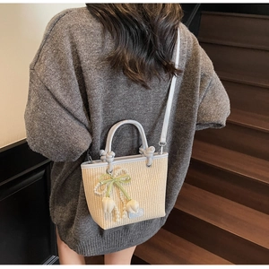 Detail of straw bucket bag with blue leather straps and pearl tulip charm on stairs