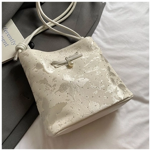 Gros plan du sac à bandoulière crème avec motif papillon et détail de breloque en perle