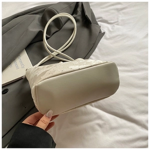 Gros plan du sac seau en dentelle crème avec ornements en perles et base en cuir