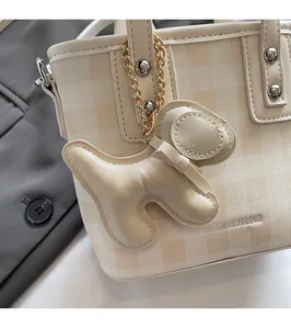 Dettaglio di un ciondolo in pelle a forma di cane su una borsa a secchiello a quadri