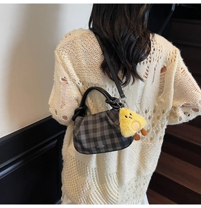 Detail of checkered mini handbag with yellow chick charm on a cream knitted sweater