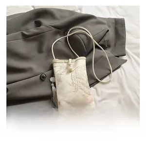 Detail of embroidered floral pattern and pearl drawstring on beige silk crossbody bag