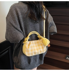 Detail of yellow checkered pleated handbag with cute chick pendant on model