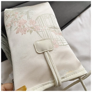 Detailed close-up of embroidered pink flowers and green patterns on an ivory phone bag