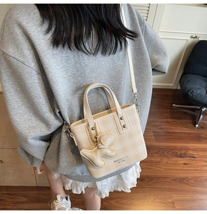 Detail of beige checkered mini bucket bag with a cute puppy charm and adjustable strap