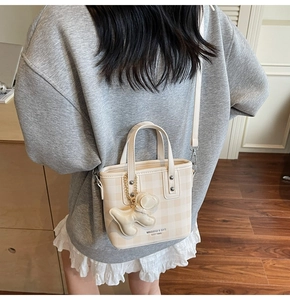 Detailed view of beige checkered bucket bag with a cute puppy pendant and gold metal hardware