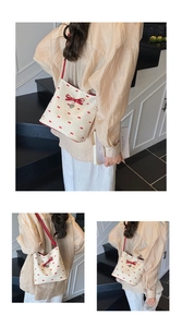 Detail of beige bucket bag with red bow prints and heart pendant in indoor setting