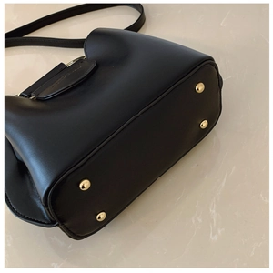 Detail view of gold-tone metal protective feet on black bucket bag's leather base