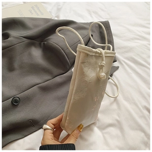 Detail of embroidered beige crossbody phone bag with floral patterns and pearl drawstring