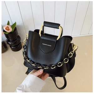 Close-up of black leather bucket bag featuring gold metal handle and chain detail