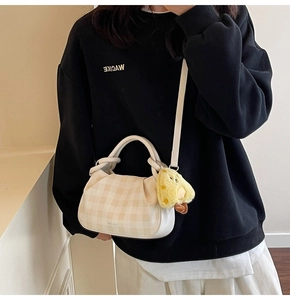 Close-up of cream checkered handbag with cute yellow plush duck charm on long strap