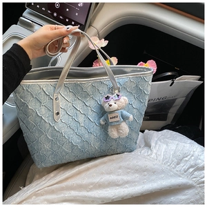 Detail of light blue pleated tote bag with silver leather handles and teddy bear charm