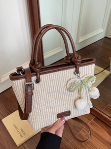 Straw bucket bag with brown leather trim and pearl tulip charm pendant in a room