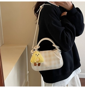 Detailed view of cream checkered crossbody bag with cute yellow chicken plush keychain