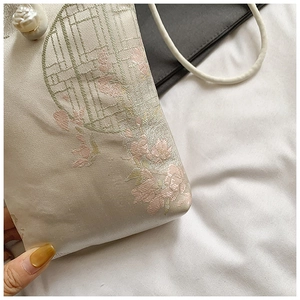 Detail of floral embroidery on a silk fabric phone bag with a pearl button closure