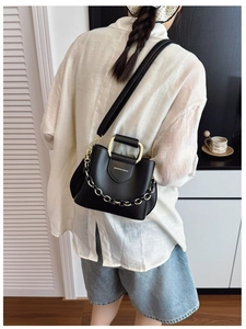 Detail view of the black bucket bag with a golden square handle and decorative chain link