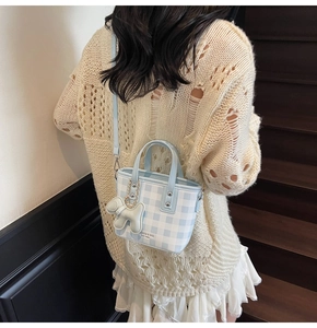 Close-up of mini checkered crossbody bag featuring a cute green puppy charm on wood stairs