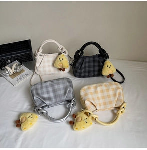 Four checkered pleat tote bags with yellow plush charms and adjustable straps on a bed