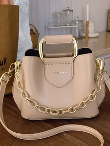 Chic beige bucket bag with wave edge design and gold square handle on a wooden desk