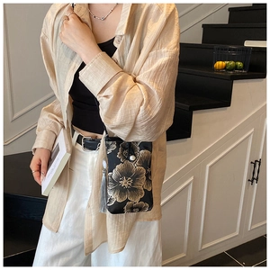 Detail view of black satin crossbody phone bag with floral embroidery and grey tassels