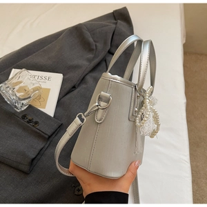Détail du sac seau argenté avec texture grain de bois et pendentif nœud en perles