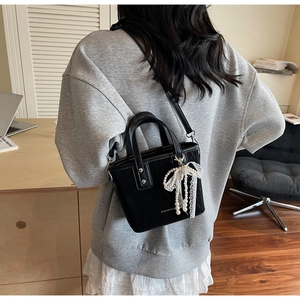 Detail of black textured crossbody bag with pearl lace bow and vertical stripe pattern
