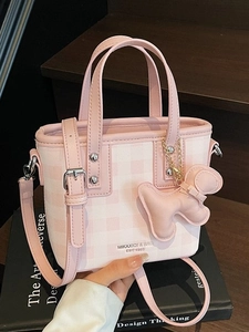 Pink checkered crossbody bucket bag with adjustable strap and cute dog charm on a book