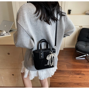 Détail du mini sac bandoulière noir avec lettrage et pendentif nœud perlé élégant