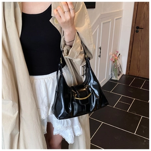 Détail du sac hobo en cuir brillant noir avec boucle dorée porté avec un trench-coat