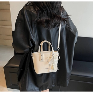 Détail d'un mini sac seau crème avec breloque nœud en dentelle et perles