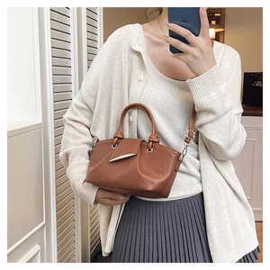 Close-up of brown pebbled leather handbag with silver clasp and side pleated details
