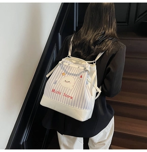 Rear view of striped canvas backpack with leather trim worn on model in a staircase setting