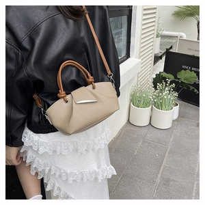 Outdoor street style view of a beige pleated handbag with brown straps and silver clasp