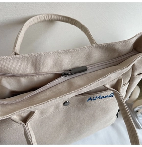 Detail of beige canvas tote bag with metal zipper and AiManQ blue letter embroidery