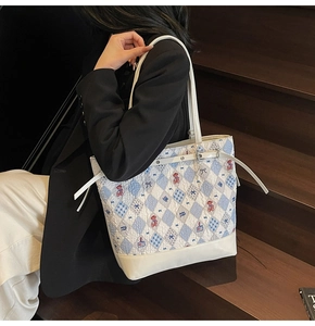Detail of blue quilted tote bag featuring red teddy bear embroidery and white leather handles