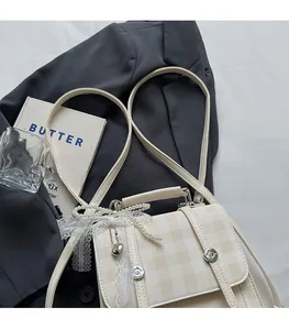 Detail of vintage beige plaid handbag featuring pearl bow and lace charms on a suit background