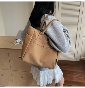 Close-up of a large tan canvas tote bag featuring an embroidered logo and side pocket detail